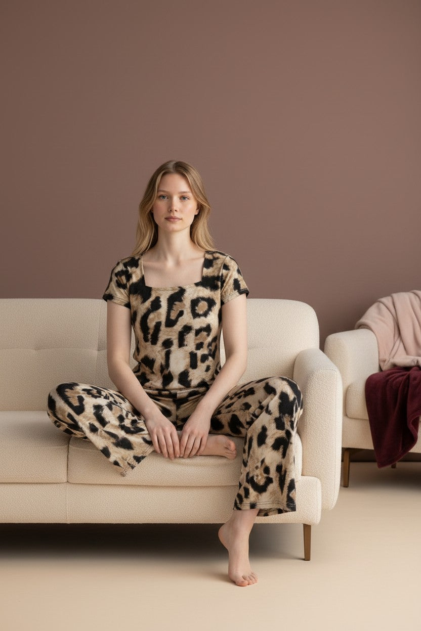 Woman wearing a pyjama leopard print lounge set with a square neckline and wide-leg pants, sitting on a beige sofa.