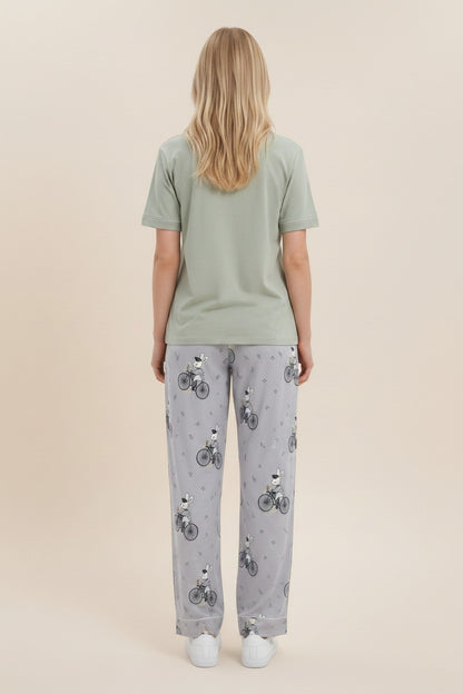 Back view of a woman wearing a pyjama olive cotton t-shirt and grey trousers with a whimsical rabbit bicycle print.