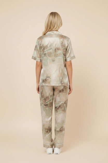 Back view of a woman wearing a pyjama soft silk pajama set with a green and beige abstract print and white piping.
